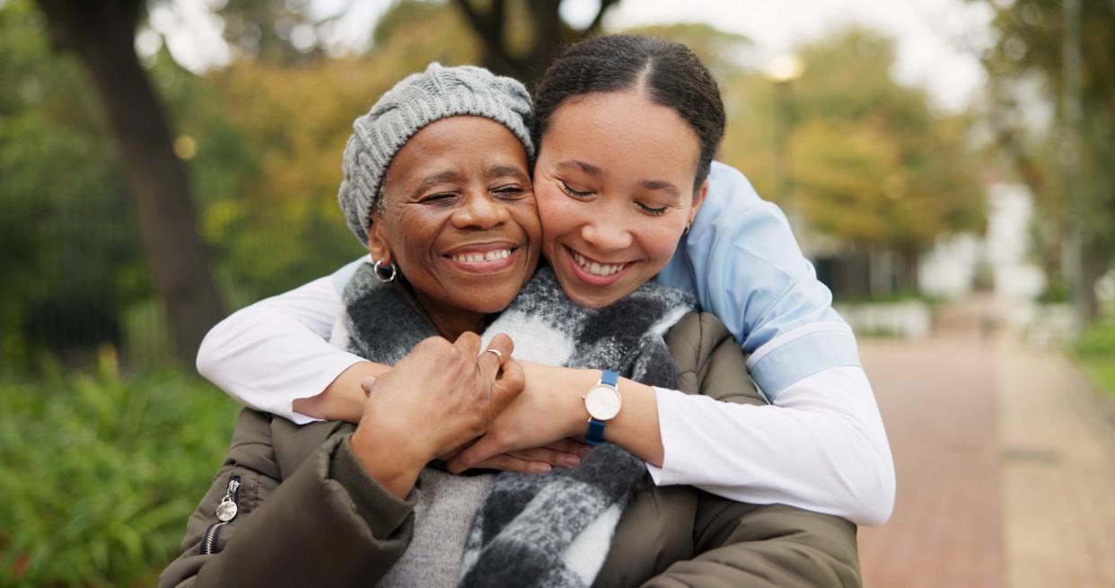 Caregiver, hug and park with old woman in a wheelchair for retirement, elderly care and physical therapy. Trust, medical and healthcare with portrait of patient and nurse in nature for rehabilitation