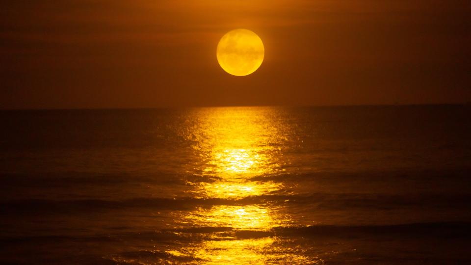 A bright full moon rises over the ocean and is reflected on the water surface