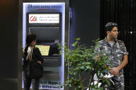 A woman uses ATM outside a bank, as a Lebanese policeman stands guard, in Beirut, Lebanon, Wednesday, Nov. 20, 2019. Lebanon’s worsening financial crisis has thrown businesses and households into disarray. Banks are severely limiting withdrawals of hard currency, and Lebanese say they don’t know how they’ll pay everything from tuitions to insurance and loans all made in dollars. Politicians are paralyzed, struggling to form a new government in the face of tens of thousands of protesters in the streets for the past month demanding the entire leadership go. (AP Photo/Bilal Hussein)