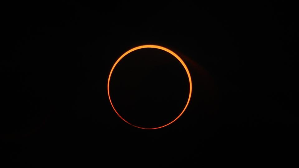 The sun looks like an orange ring against a black sky.