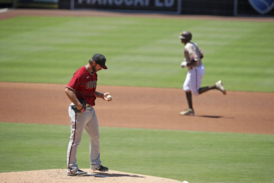 Madison Bumgarner in a red jersey holding a ball on the mound while Manny Machado jogs to second behind him. 