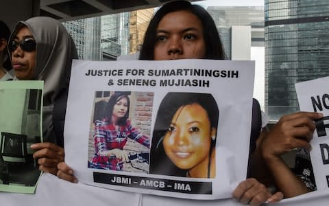 A migrant worker holds up a piece of paper showing photos of Sumarti Ningsih (L) and Seneng Mujiasih (R), both in their 20s, who were found dead in British banker Rurik Jutting's Hong Kong apartment  - Credit: AFP