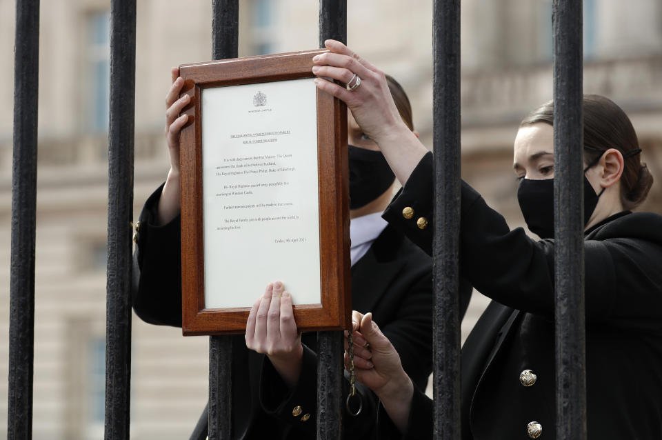 Personal del Palacio de Buckingham coloca un anuncio oficial de la muerte del príncipe Felipe en la entrada, en Londres, el viernes 9 de abril de 2021. Felipe, el esposo de la reina Isabel II, tenía 99 años. (AP Foto/Matt Dunham)
