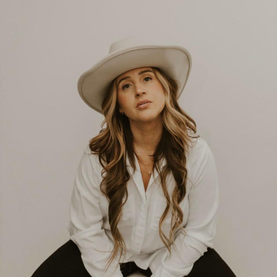 Woman in a white shirt and wide-brimmed hat sitting on a stool