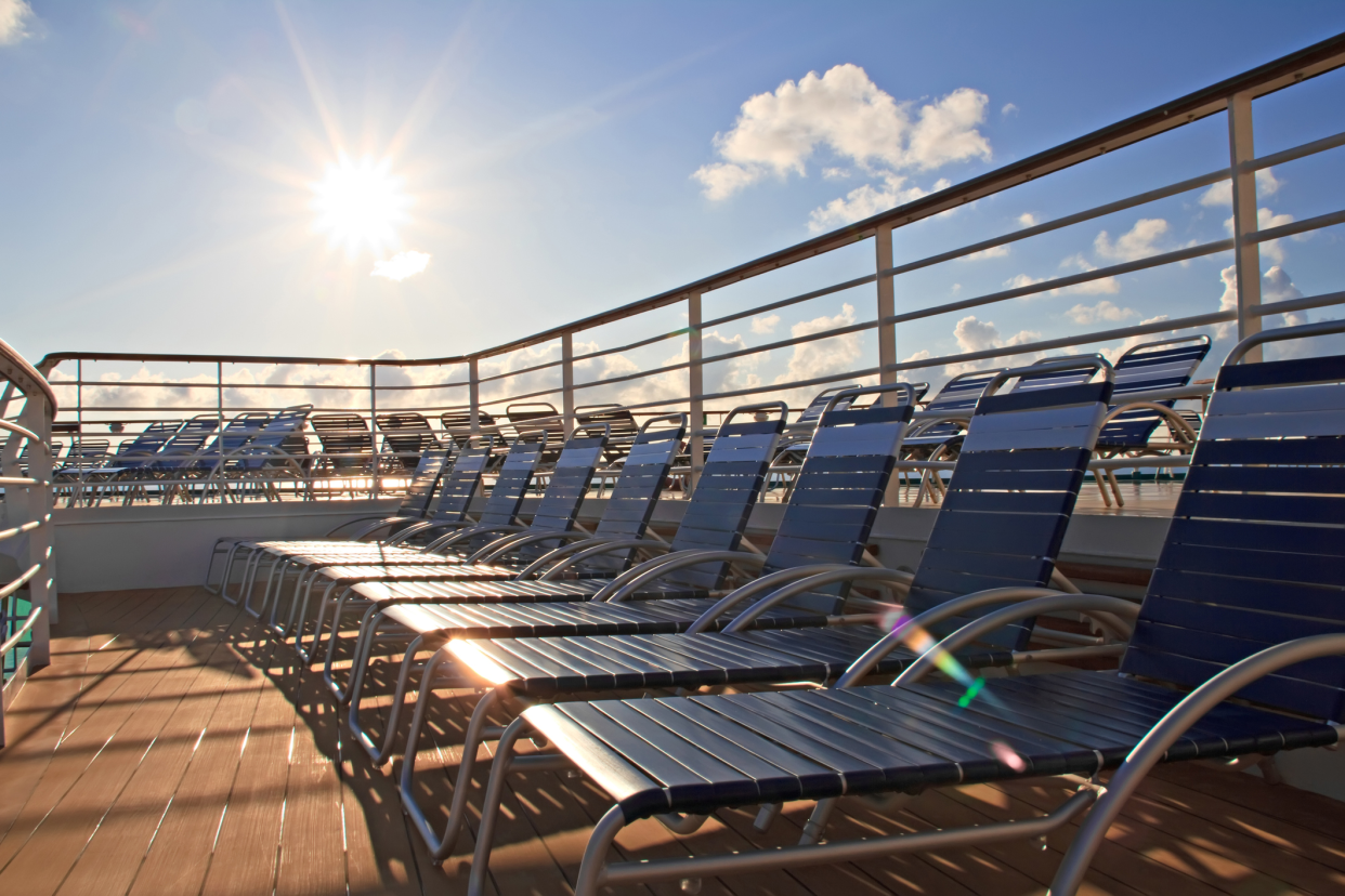 Many rows of lounge chairs on the deck of cruise ship, one row in the foreground, bright sun in the sky shining