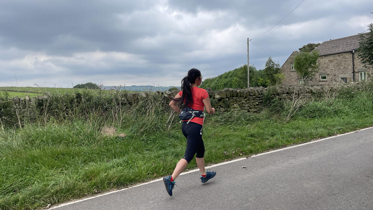  A woman runs down a country road, a Black Diamond Pursuit Waist Pack 6L around her waist. 