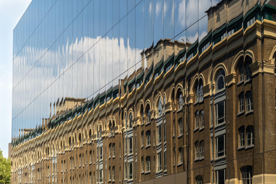 New versus old - an old brick building reflected in windows of modern new facade