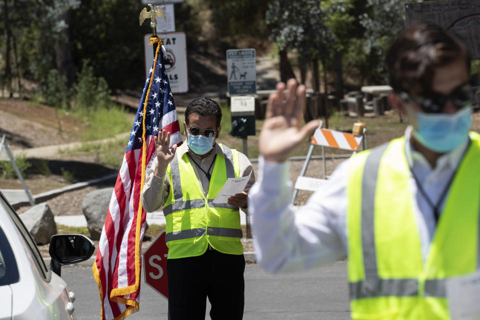 In this June 26, 2020 photo, Immigration Service Officer Bay, left, leads an oath in front of Immigration Service Officer Coronel, right, during a drive-in citizenship ceremony in El Cajon, Calif. The path to becoming a U.S. citizen, and a new voter, had already become longer under President Donald Trump when COVID-19 brought it virtually to a halt. Smaller naturalization ceremonies have resumed -- under socially distant rules that turn a once-joyous and patriotic occasion into something more like a visit to a fast-food restaurant -- but could soon stall again as the nation's citizenship agency faces an unprecedented budget shortfall and the possibility of a furlough for nearly three-fourths of its workforce. (AP Photo/Gregory Bull)