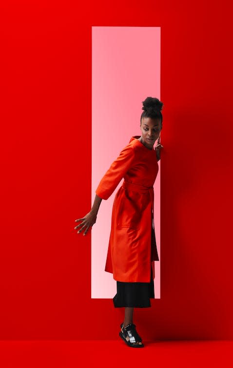 A Black woman wearing red comes out of a pink window