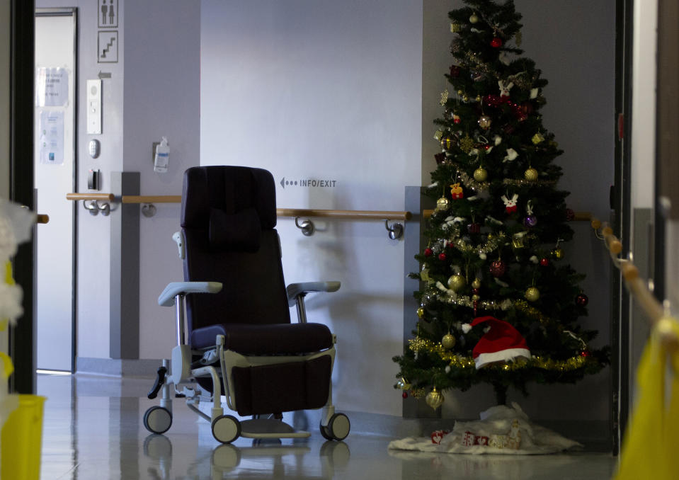 An empty chair is left in a hallway next to a Christmas tree in the COVID-19 ward at the St. Michiel Hospital in Brussels, Tuesday, Nov. 24, 2020. Nations are struggling to reconcile cold medical advice with a holiday tradition that calls for big gatherings in often poorly ventilated rooms, where people chat, shout and sing together, providing an ideal conduit for a virus that has killed over 350,000 people in Europe so far. (AP Photo/Virginia Mayo)