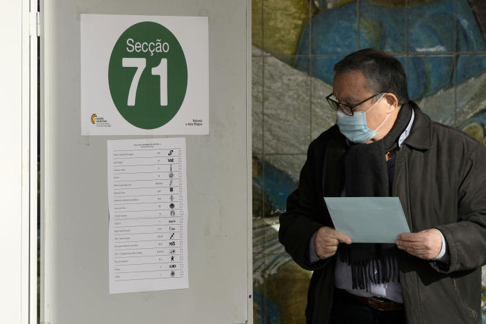 A man wearing a face mask and holding the envelope with his ballot paper looks at a ballot sample pasted on a voting booth at a polling station for early voters in Portugal's general election, at the University of Lisbon, Sunday, Jan. 23, 2022. Portuguese voters go to the polls Sunday, two years earlier than scheduled after a political crisis over a blocked spending bill brought down the country's minority Socialist government and triggered a snap election. (AP Photo/Armando Franca)