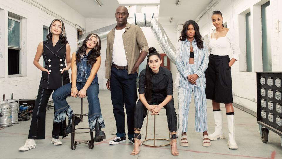 Six people, five women and one man, sit and stand facing the camera backstage at a TV studio