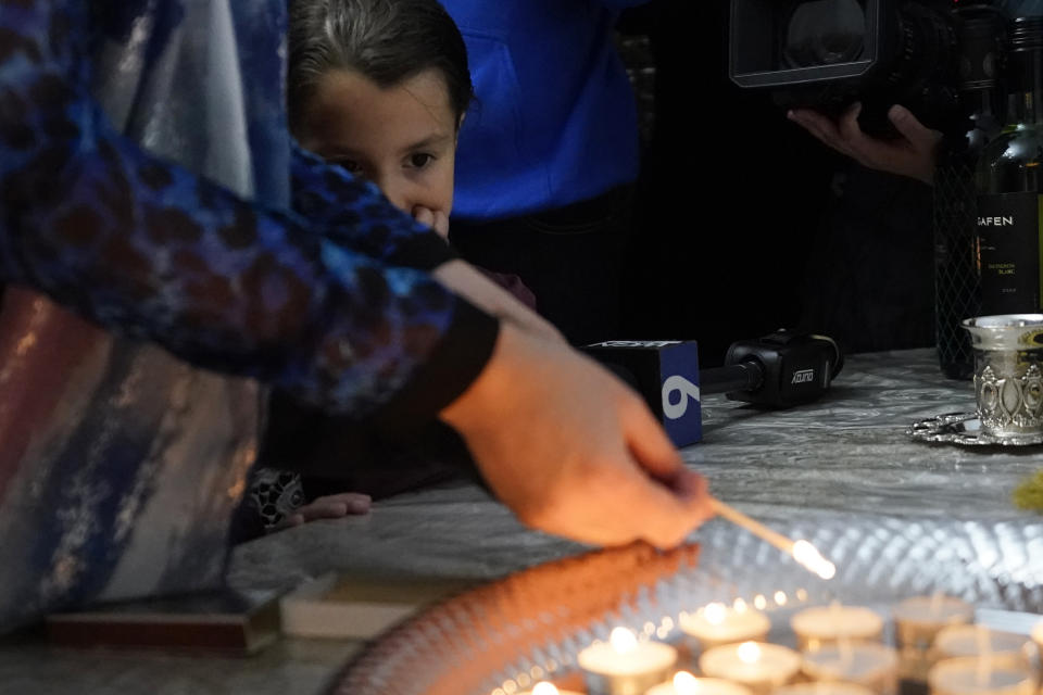 Yehudis Hecht's daughter Chana, watches her mother lights candles to mark the beginning of Shabbat on Friday, Oct. 20, 2023, in Evanston, Ill. Judith Raanan, a member of Chabad, and her daughter Natalie were released Friday from their captivity in Gaza. (AP Photo/Charles Rex Arbogast)