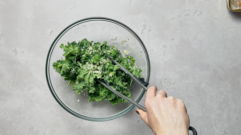 tossing kale with dressing with tongs