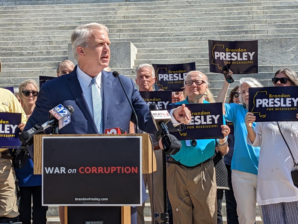 Brandon Presley at the microphone with a crowd supporters behind him holding placards with his name and a poster on the podium saying : War on Corruption.