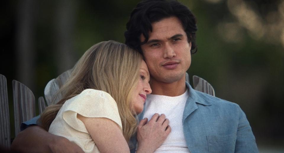 Charles Melton and Julianne Moore embrace on a bench, with Julianne resting her head on Charles's shoulder, in an intimate and serene moment