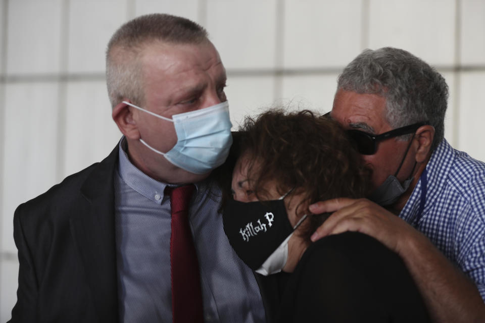 Magda Fyssa, center, and Panagiotis Fyssas, right, the parents of late Greek rap singer Pavlos Fyssas, who was stabbed and killed by a supporter of the extreme right Golden Dawn party in 2013 triggering a crackdown on the party, are escorted into the court by their attorney Andreas Tzelis, in Athens, Wednesday, Oct. 7, 2020. The court is to deliver a landmark verdict in the marathon, five-year-long trial against the country's extreme right-wing Golden Dawn party Wednesday, with security tight and anti-fascist rallies outside the court for the politically charged case. (AP Photo/Petros Giannakouris)