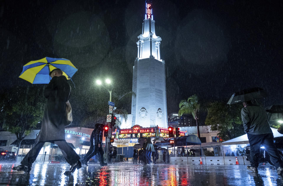 People walk in the rain past the Fox Theater before the premier of Bob Marley: One Love Tuesday, Feb. 6, 2024, in the Westwood area of Los Angeles. (AP Photo/Ethan Swope)