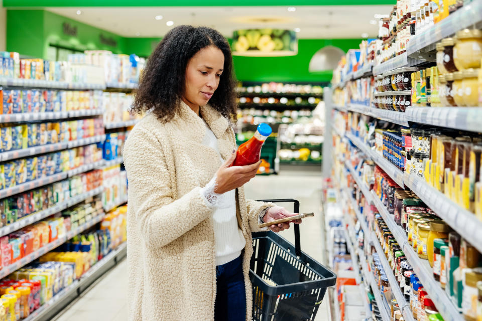 A woman standing in an isle in her local supermarket and reading the product label of an item while out grocery shopping.