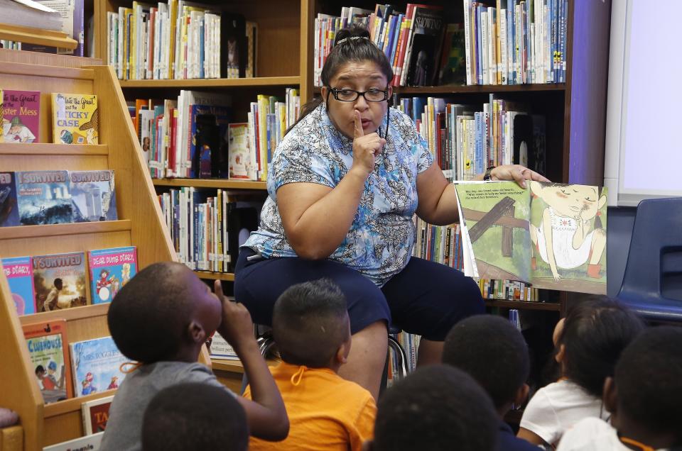 Librarian Luz Ochoa, top, interacts with Mike Nkurunziza, left, as Ochoa reads to the students at Valencia Newcomer School in the library Thursday, Oct. 17, 2019, in Phoenix. Children from around the world are learning the English skills and American classroom customs they need to succeed at so-called newcomer schools. Valencia Newcomer School in Phoenix is among a handful of such public schools in the United States dedicated exclusively to helping some of the thousands of children who arrive in the country annually. (AP Photo/Ross D. Franklin)