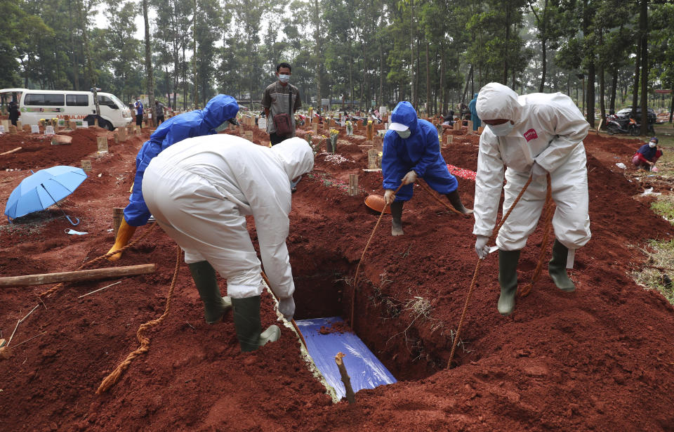 In this July 14, 2021, photo, workers in protective gear lower a coffin of a COVID-19 victim to a grave for burial at the Cipenjo Cemetery in Bogor, West Java, Indonesia. Images of bodies burning in open-air pyres during the peak of the pandemic in India horrified the world in May, but in the last two weeks Indonesia and two other Southeast Asian nations have surpassed India’s peak per capita death rate as a new coronavirus wave tightens its grip on the region. (AP Photo/Achmad Ibrahim)