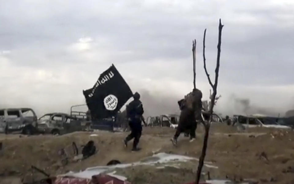 This frame grab from video posted online Monday, March 18, 2019, by the Aamaq News Agency, a media arm of the Islamic State group, shows IS fighters walking as they hold the group's flag inside Baghouz, the Islamic State group's last pocket of territory in Syria. U.S.-backed Syrian forces fighting the Islamic State group announced Tuesday they have taken control over an encampment in an eastern Syrian village where IS militants have been besieged for months, refusing to surrender. (Aamaq News Agency via AP)