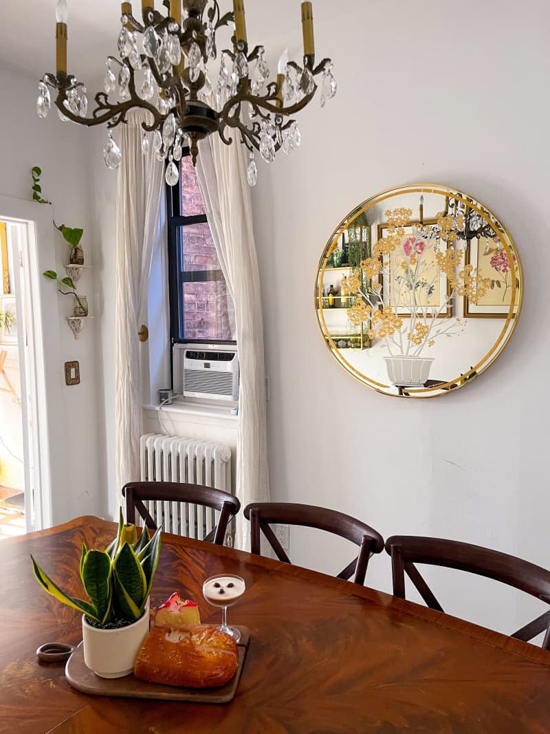 Large wooden dining room table under a chandler and large vintage circular mirror