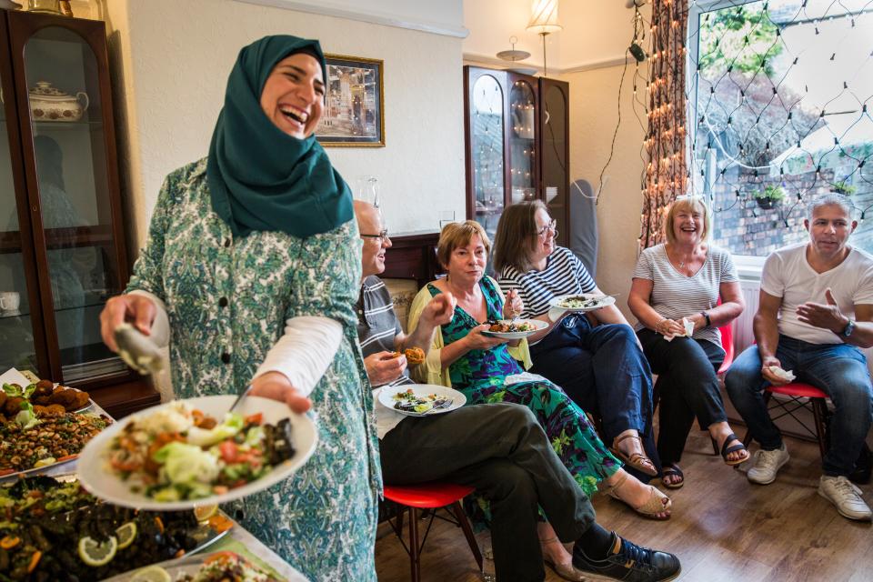 <p>Ghofran Khaled Jhayem (left) and her husband Ismael share Syrian food with members of their community support group at the family's new home in Liverpool</p> (Andrew McConnel)