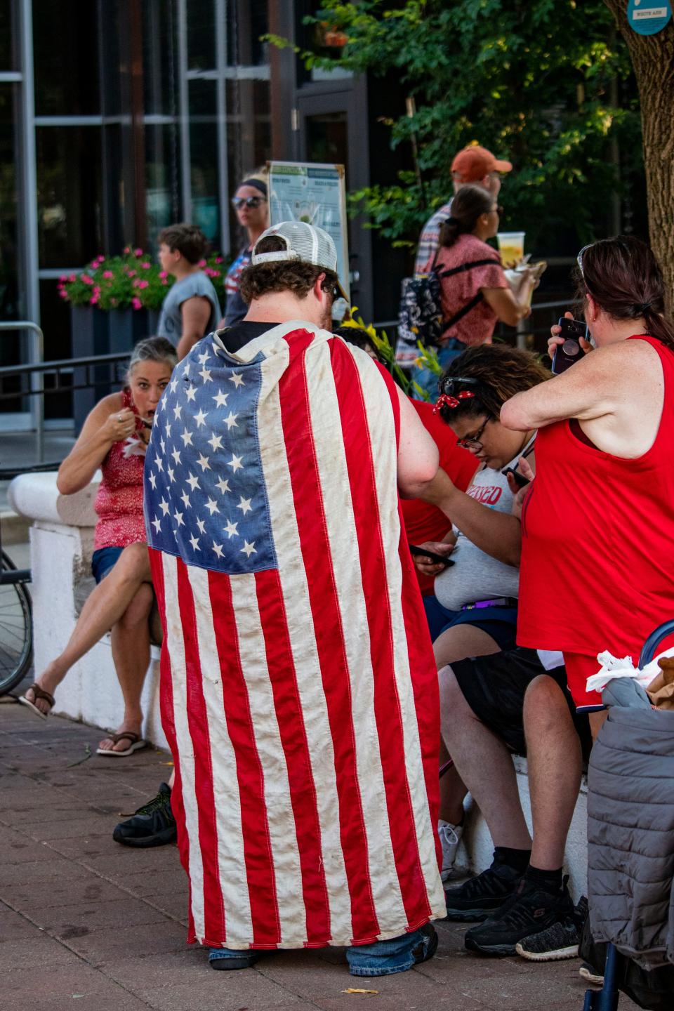 A man wears an American Flag July 4, 2021, in downtown Lafayette, Ind., as attendees enjoy the musical performances of the Stars & Stripes Celebration. People gathered around to celebrate the Fourth of July before the fireworks show.