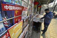 A newsstand vendor looks through his display near a magazine with a cover depicting U.S. President Joe Biden near U.S. and Chinese flags in Beijing on Thursday, Jan. 21, 2021. As a new U.S. president takes office, he faces a determined Chinese leadership that could be further emboldened by America's troubles at home. (AP Photo/Ng Han Guan)