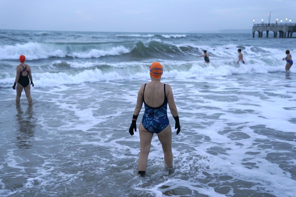 Swimmers make their way out to sea as the sun begins to rise over Boscombe beach in Dorset. Picture date: Saturday January 1, 2022. (PA Archive)