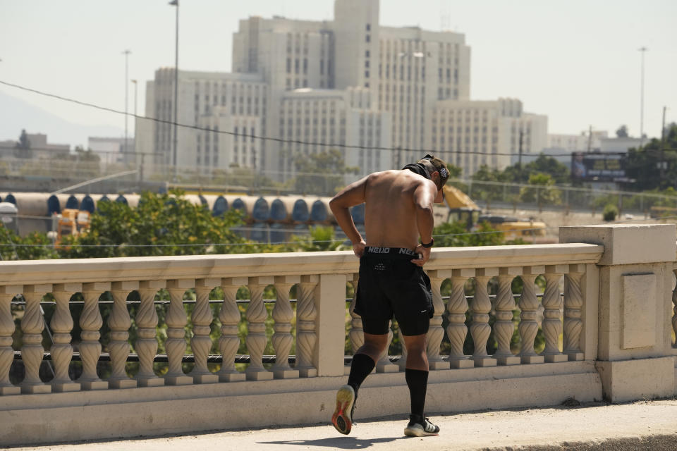 A runner walks across the Los Angeles River on the Cesar Chavez Avenue Bridge in Los Angeles, Thursday, July 13, 2023. After a historically wet winter and a cloudy spring, California's summer was in full swing Thursday as a heat wave that's been scorching much of the U.S. Southwest brings triple digit temperatures and an increased risk of wildfires. In the background, the Los Angeles General Medical Center. (AP Photo/Damian Dovarganes)