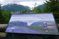 Exit Glacier is seen in the distance, behind a park sign depicting the Glacier face as seen in 2011, at Kenai Fjords National Park, Alaska