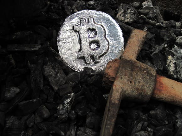 pickaxe and silver coin with bitcoin symbol on it lying on a pile of coal