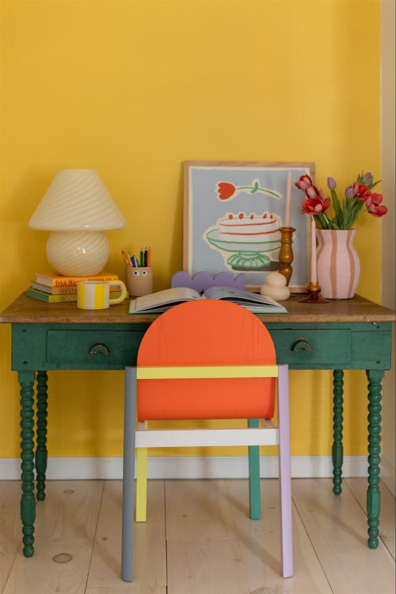 Yellow painted wall in colorful workspace with color block painted desk chair.