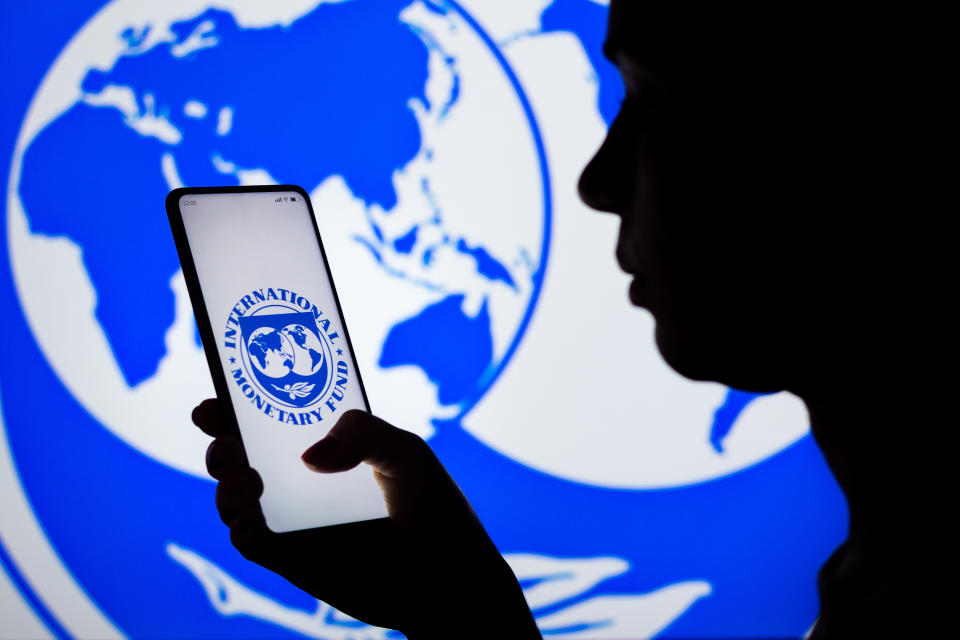 BRAZIL - 2022/04/06: In this photo illustration, a woman's silhouette holds a smartphone with the International Monetary Fund (IMF) logo displayed on the screen and in the background. (Photo Illustration by Rafael Henrique/SOPA Images/LightRocket via Getty Images)