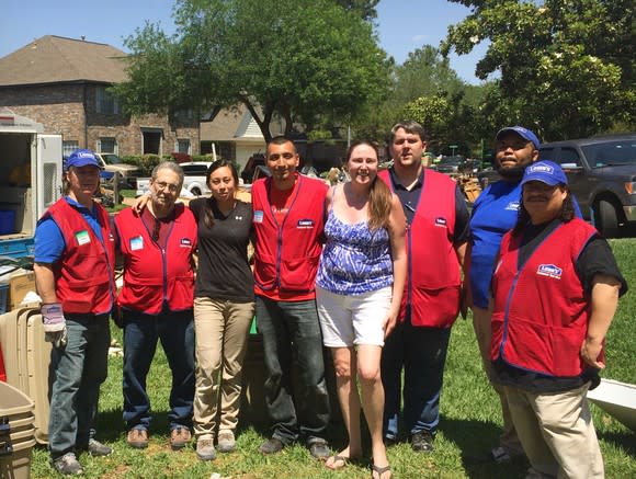 Lowe's employees gathered on a lawn in a residential neighborhood helping a family.