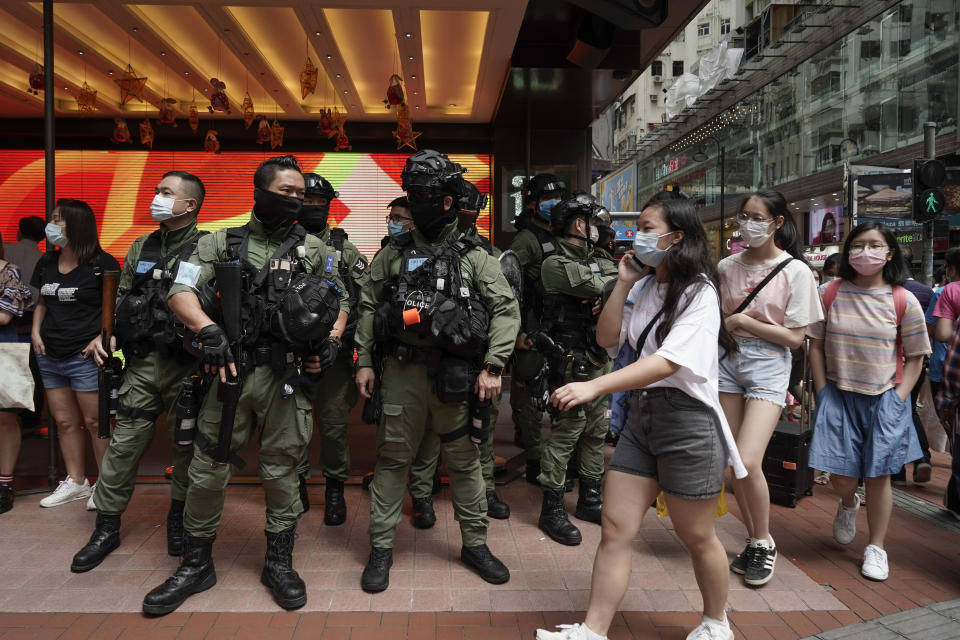 Pedestrians pass police standing guard during China's National Day in Causeway Bay, Hong Kong, Thursday, Oct. 1, 2020. A popular shopping district in Causeway Bay saw a heavy police presence the Oct. 1 National Day holiday despite low protester turnout. (AP Photo/Kin Cheung)