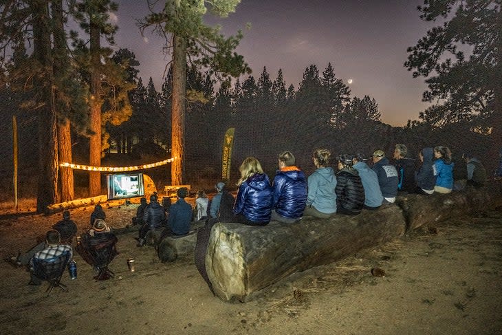 hikers sitting on logs and watching a movie at night