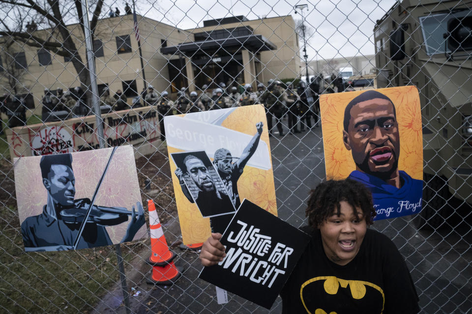 A demonstrator holds a sign along a perimeter fence guarded by law enforcement officers during a protest over Sunday's fatal shooting of Daunte Wright during a traffic stop, outside the Brooklyn Center Police Department, Wednesday, April 14, 2021, in Brooklyn Center, Minn. At right on the fence is an image of George Floyd. (AP Photo/John Minchillo)