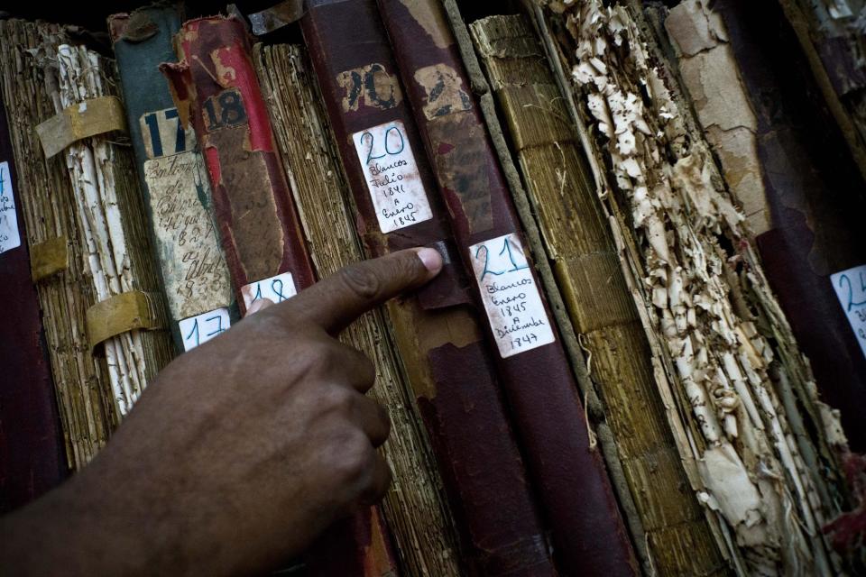 This Jan. 12, 2017 photo shows a man searching among volumes labeled "Whites" as part of an effort to digitize colonial-era registries of blacks and whites at the Espiritu Santo Church in Old Havana, Cuba. "That's how these books where placed, books for whites, books for blacks. The important thing is to preserve as many of them as possible,” said church Deacon Felix Knights. (AP Photo/Ramon Espinosa)