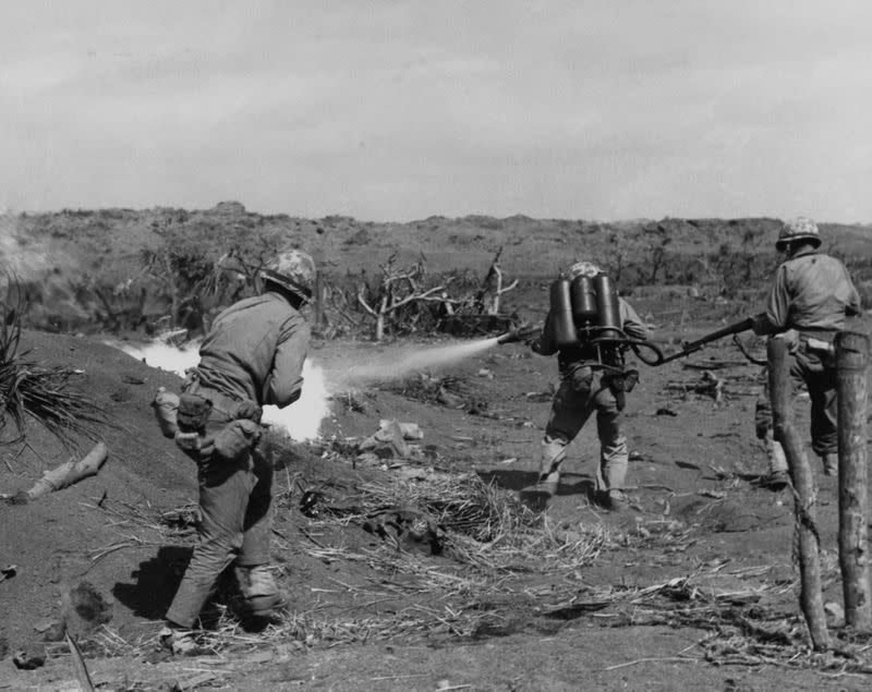 A U.S. Marine flame thrower operator in action, covered by a pair of riflemen, on Iwo Jima