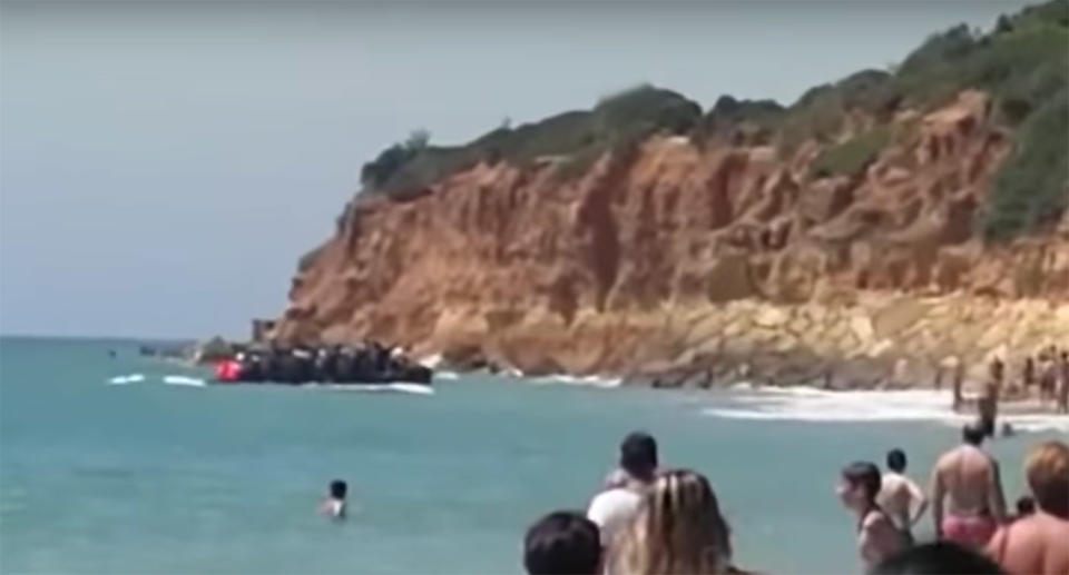 Stunned tourists watched as a boat load of migrants landed at a popular Spanish beach and quickly scrambled up nearby cliffs at Barossa beach in Cadiz, Spain.