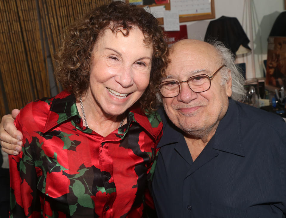 Rhea Perlman and Danny DeVito smiling together, with Rhea wearing a floral patterned shirt and Danny in a casual button-up