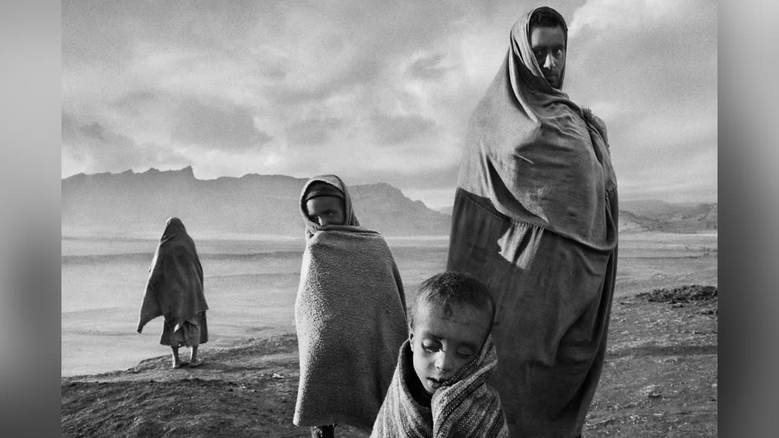  Draped in blankets to keep out the cold morning wind, refugees wait outside Korem camp. Ethiopia, 1984. © Sebastião Salgado. 