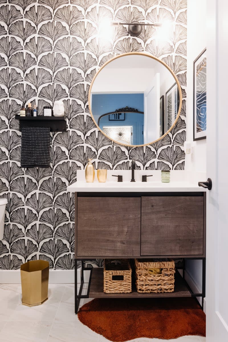 Bathroom with black and white gingko leaf print wallpaper, circle mirror, and wood sink cabinet