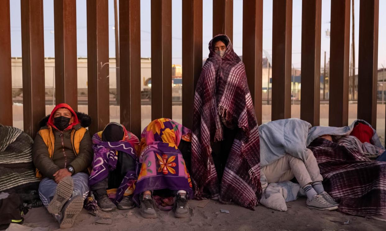 <span>Asylum seekers bundle up against the cold after spending the night outside along the US-Mexico border fence in December 2022.</span><span>Photograph: John Moore/Getty Images</span>