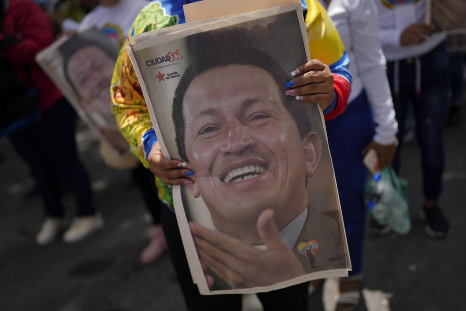 A visitor holds a poster with the image of late Venezuelan President Hugo Chavez as she lines up to visit Chavez's tomb, during commemorations marking the tenth anniversary of his death, at the Cuartel de la Montaña 4F where his remains are interred in Caracas, Venezuela, Sunday, March 5, 2023. Chavez died on March 5, 2013, after a long battle with cancer and chose current president, Nicolas Maduro, a former bus driver and union leader to be his successor. (AP Photo/Ariana Cubillos)