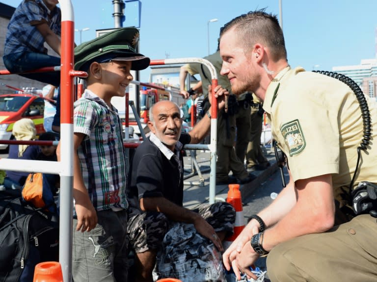 A German police officer and a migrant boy joke with the officer's cap while migrants wait for a bus after their arrival at the main train station in Munich, southern Germany, September 1, 2015