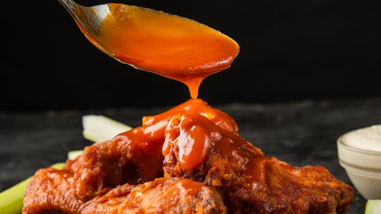 spooning buffalo sauce over wings